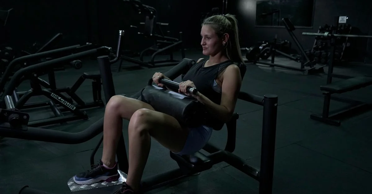 Une femme effectue des exercices pour les jambes sur une machine de gymnastique dans un environnement faiblement éclairé.
