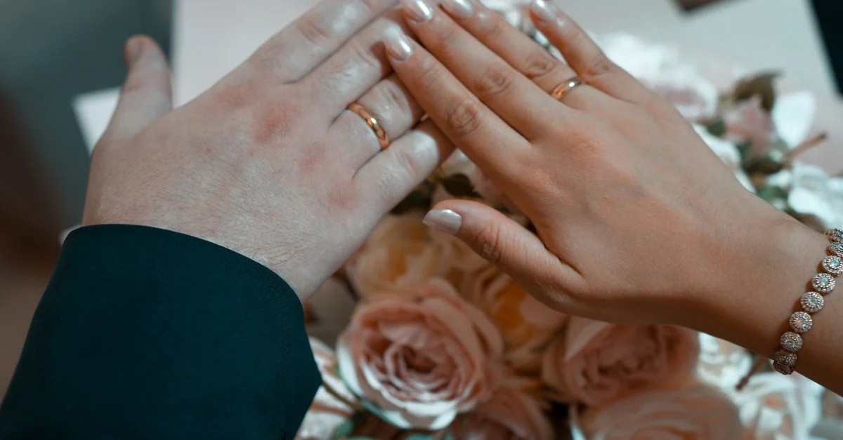 Mains avec des alliances sur un bouquet de roses roses, symbolisant l'amour et l'engagement.