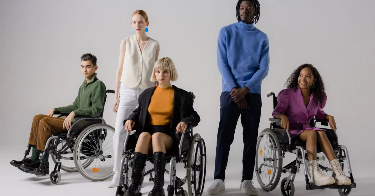 Un groupe de modèles divers montrant la mode inclusive avec des fauteuils roulants dans un studio.