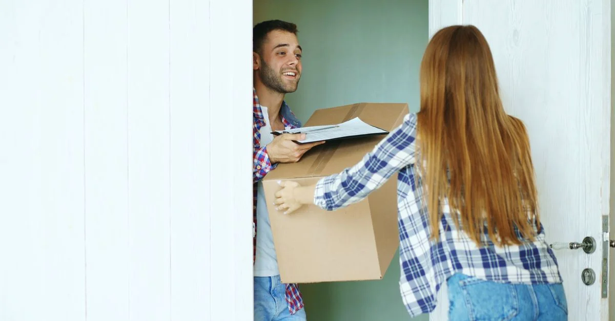 Un jeune couple déménageant heureux dans sa nouvelle maison, portant des cartons à la porte d'entrée.