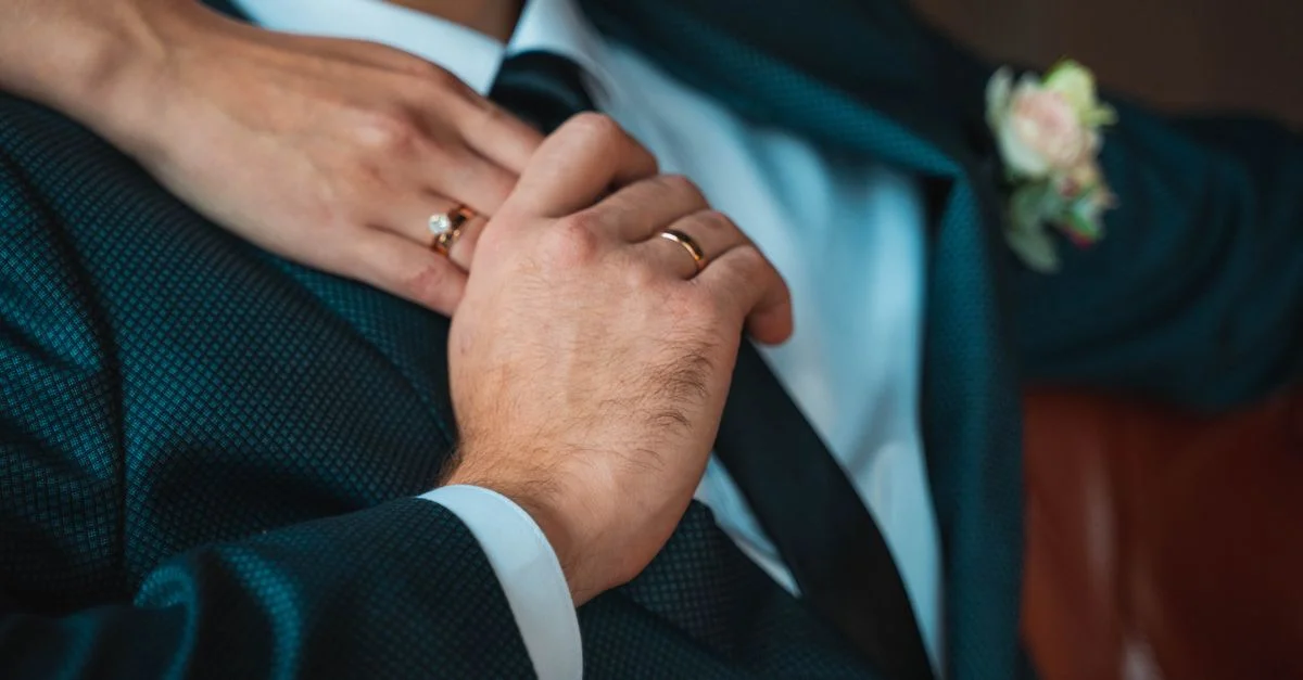 Gros plan d'un marié ajustant sa cravate tout en tenant la main de la mariée, mettant en valeur les alliances.