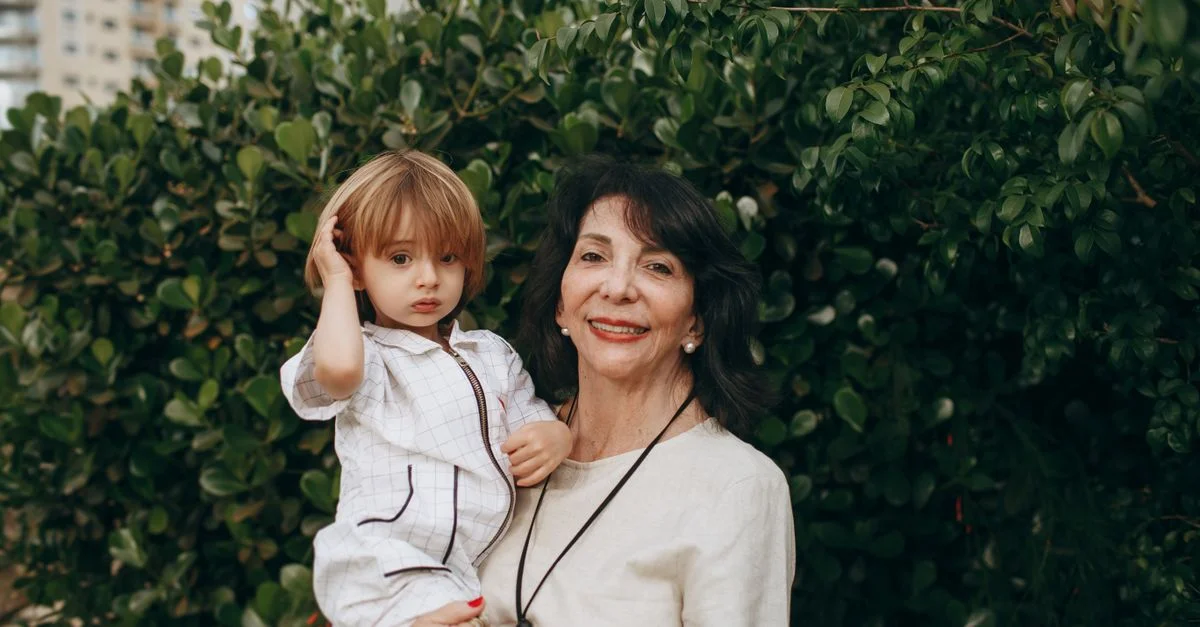 Une grand-mère aimante avec son petit-enfant souriant en plein air dans un jardin luxuriant.